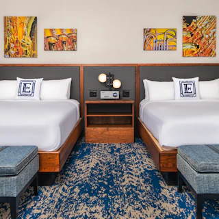 Elkhart County Hotel room with two double beds, wooden headboards, blue patterned carpet, musical instrument artwork, and blue upholstered benches.