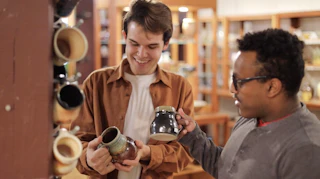 Visitors browsing handmade pottery on display shelves inside a local artisan shop, examining ceramic mugs and bowls in Elkhart County, Indiana.