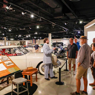 A small group listening to a tour guide, with cars in display at the Studebaker National Museum in South Bend, IN