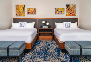 Elkhart County Hotel room with two double beds, wooden headboards, blue patterned carpet, musical instrument artwork, and blue upholstered benches.